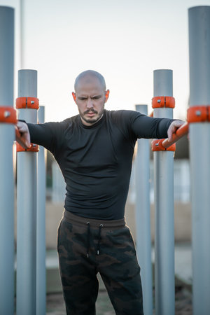 A young Hispanic man having a rest after exercising on the horizontal bars