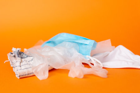 A top view shot of used disposable gloves and a surgical facemask isolated on an orange backgroundの写真素材