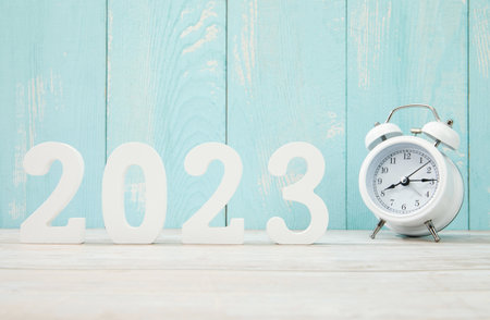 '2023' made with plastic numbers and an alarm clock on a blue wooden background.