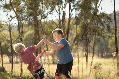 The two brothers playing on a rope swing in a beautiful bush locationの写真素材