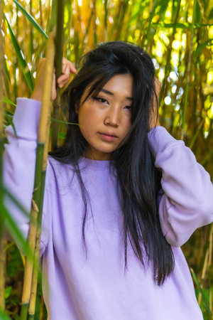 A vertical shot of a beautiful Chinese girl's portrait, posing near bamboo plants, outdoors during daylightの写真素材