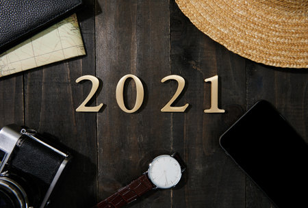 A camera, watch, smartphone, wallet, map and 2021 made with plastic numbers on a wooden tableの写真素材