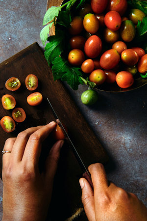 A top view of a person cutting fresh cherry tomatoes on a wooden board on the tableの写真素材