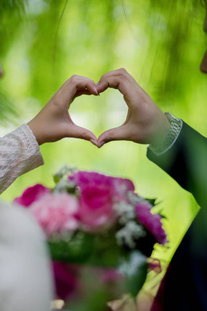 A vertical shot of a bride and a groom holding a heart with their handsの写真素材