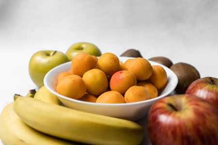 A closeup shot of apricots in the bowl with fresh apples bananas and kiwisの写真素材