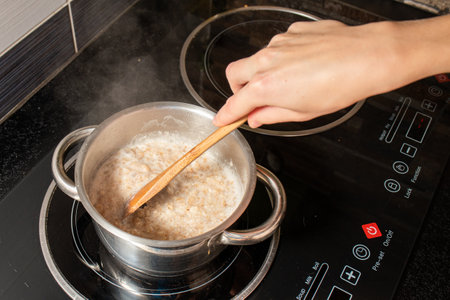 A high angle shot of a person cooking oatmeal with milk in a pot on the stoveの写真素材