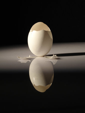 A vertical shot of a cracked empty egg shell reflecting on the table under the lightsの写真素材