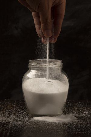 A vertical shot of a person throwing a pinch of salt in a jar against a dark backgroundの写真素材