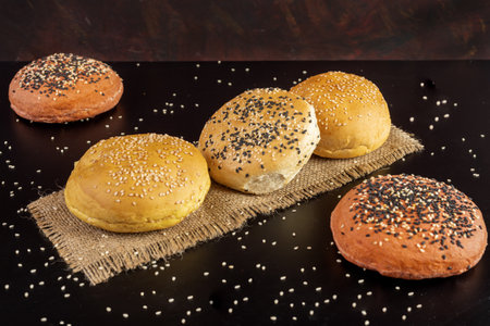Tasty freshly baked hamburger buns with grains on a black background