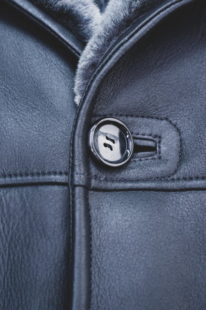 A vertical closeup of the button on a beautifully textured, navy blue leather jacket