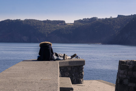 A selective focus shot of a young loving couple sitting on a stone wall on a lak