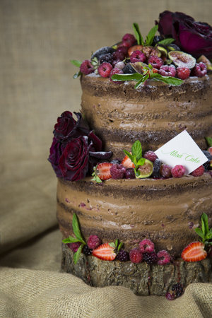 A vertical closeup shot of a delicious chocolate cake with fruits and roses