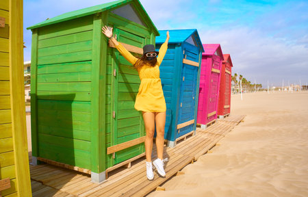 A Caucasian girl in a mask jumping on the colorful beach sheds background - the concept of joy in "new normal" conditionsの写真素材