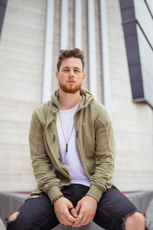 A vertical shot of a handsome young Caucasian man, wearing ripped jeans and a jacket, posing...