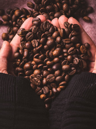 A vertical shot of a person holding roasted fresh coffee beans under the lights