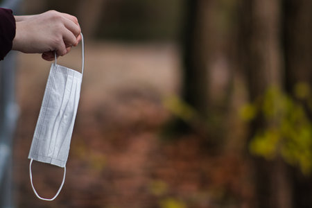 A closeup shot of a hand trowing used face mask to trashの写真素材