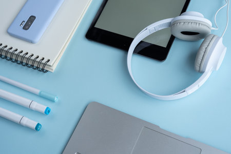 A high-angle shot of a laptop, markers, notebook, mobile phone, tablet and headphones on a blue deskの写真素材