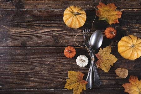 A top view of fresh pumpkins, walnuts, autumn leaves with a fork and spoon on a wooden backgroundの写真素材