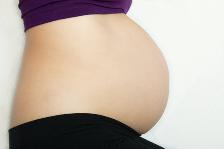 A caucasian-skinned pregnant woman with her bare belly lying on her right profile in the foreground.