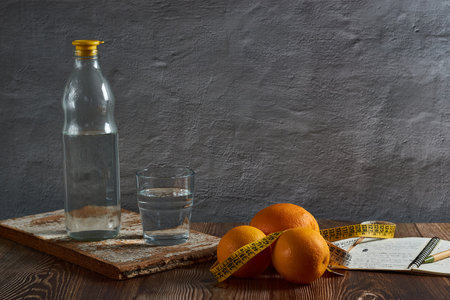 Fresh oranges, a yellow measuring tape and a glass of water on a wooden table - diet conceptの写真素材