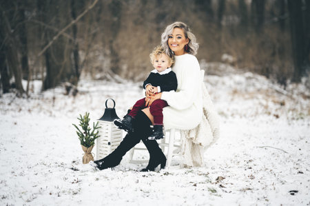 A young mother sitting on a chair outdoors with her son on her lapの写真素材