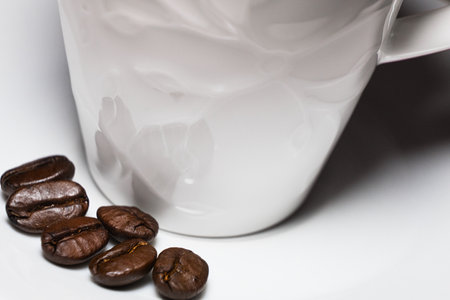 roasted coffee beans on a white clean saucer and a cup of espressoの写真素材