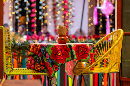 An empty Mexican restaurant table covered with a blanket with roses and yellow chairs next to itの写真素材