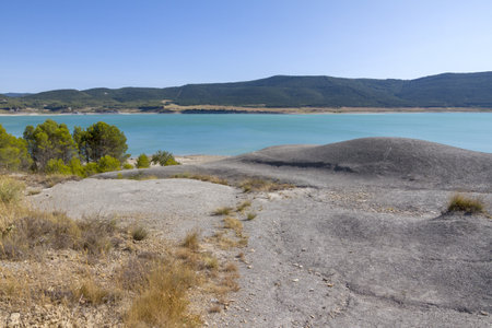 A blue clear sky over a calm river with a rocky shoreの写真素材