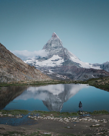 A vertical shot of a person standing by the Riffelsee Lake in the Matterhorn mountains in Switzerlandの写真素材