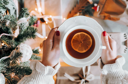 A top view of a female holding a cup of tea with lemon next to a Christmas treeの写真素材