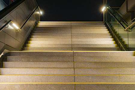 A low angle closeup of stairs with yellow lining and metallic rails with lights at night