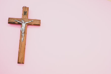 A closeup shot of a wooden crucifixion of Christ cross on a pink backgroundの写真素材