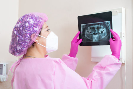 A shot of a female dentist in a medical mask examining a dental x-ray