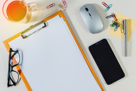 An office file folder clipboard with white paper for inscription and other office supplies on deskの写真素材