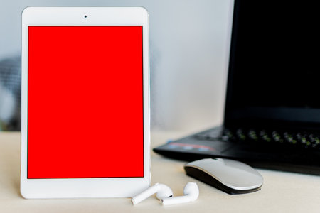 A tablet with red screen next to a laptop on a desk - technology and business conceptの写真素材