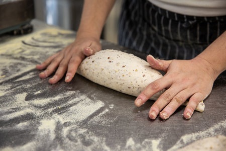 A closeup of baker's hands rolling out the bread dough on the tableの写真素材