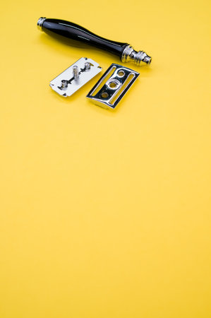 A vertical shot of a mechanical razor and blade isolated on yellow background