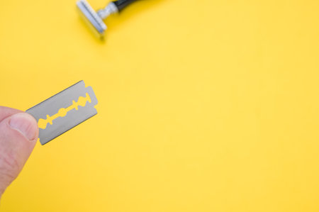 A hand holding blade with a mechanical razor on the background against a yellow surface