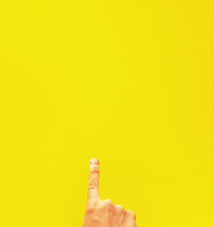 A closeup of a person pointing up isolated on a yellow background with space for teの写真素材