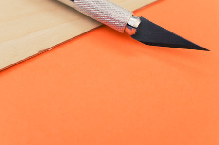A high angle shot of the metallic scalpel on a plywood surface isolated on orange background