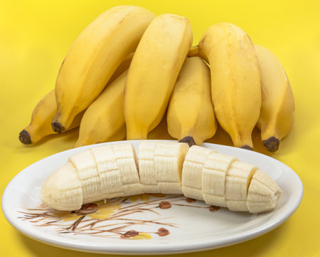 A closeup shot of chopped bananas and a bundle of ripe bananas on a yellow surfaceの写真素材