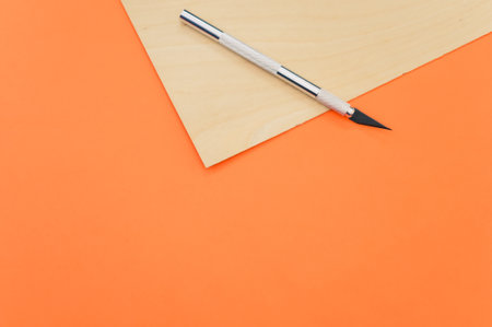 A high angle shot of the metallic scalpel on a plywood surface isolated on orange backgroundの写真素材