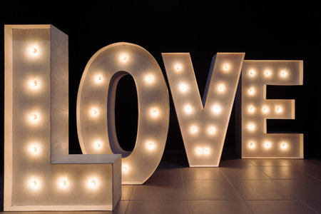 Letters illuminated with light bulbs forming the word love in an event room on a black background. Valentine's Day concept.Wedding decorations.の写真素材