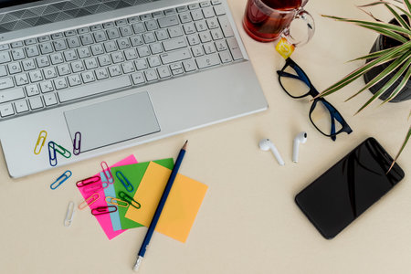 A top view of a laptop on the table with colorful notes, paper clips, and headphones with a phone on...