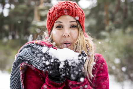 happy young woman playing with snow in winter, blowing snowflakes to camera, copy spaceの写真素材