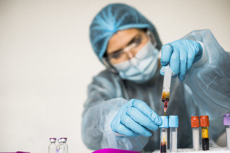Female scientist wearing highly protective suit, gloves, mask and glasses holding a tube showing...