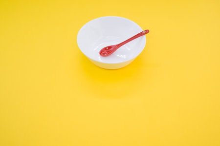 A high angle shot of a red spoon in a white bowl on a yellow backgroundの写真素材