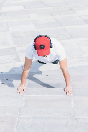 A vertical shot of a young attractive male doing pushups outdoors with headphones