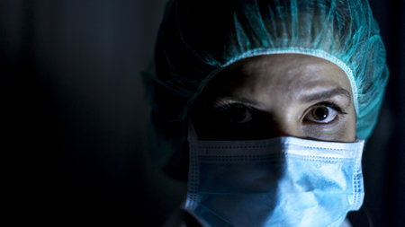 A closeup of a female healthcare worker wearing a mask on a black backgroundの写真素材