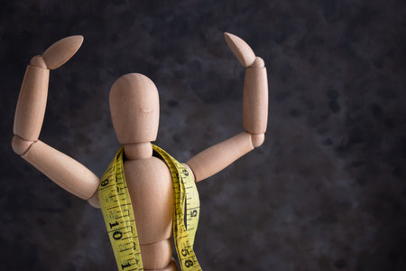 A wooden puppet with hands up and centimeter tape on the neck - the concept of sports and fitness